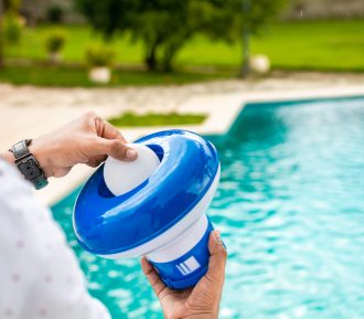 Pool float and chlorine tablets for pool maintenance. Hands holding a pool chlorine dispenser. Hand of a pool disinfection worker holding a dispenser with a chlorine tablet. Hands holding a dispenser with pool chlorine tablet